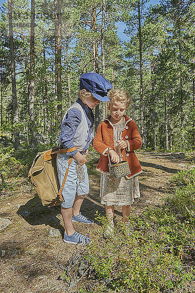 Junge und Mädchen in Retro-Kleidung beim Beerenpflücken im Wald