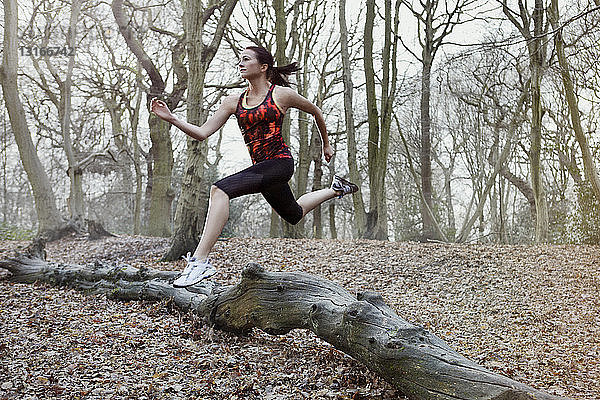Junge Frau springt im Wald über Baumstamm