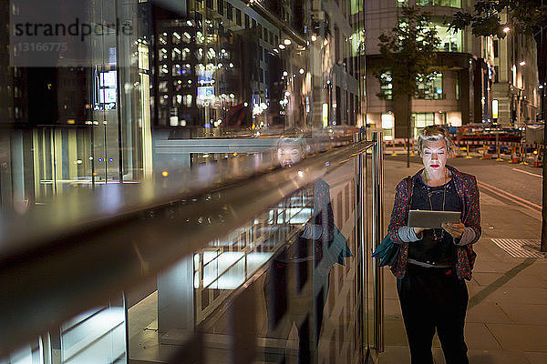 Reife Frau mit digitalem Tablet unterwegs bei Nacht  London  UK