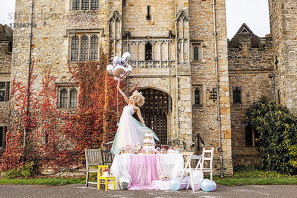 Braut steht auf einem Tisch vor dem Schloss und hält Luftballons