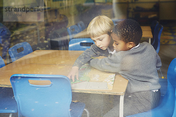 Fensteransicht von zwei Jungen beim Puzzeln am Schreibtisch im Klassenzimmer der Grundschule