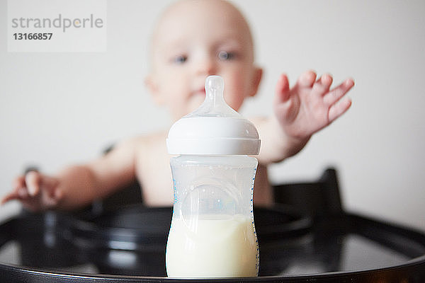 Baby Junge sitzt im Hochstuhl und greift nach der Babyflasche