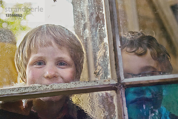 Porträt von zwei Jungen  die durch ein Hüttenfenster schauen