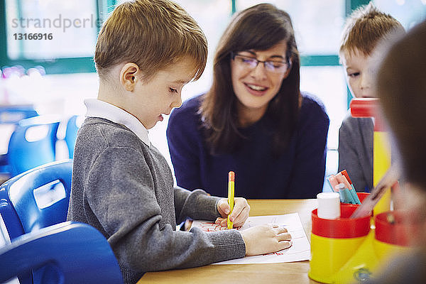 Jungen und Mädchen mit Lehrer zeichnen am Schreibtisch in der Grundschule