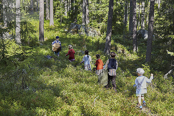 Sechs in Retro-Kleidung gekleidete Jungen und Mädchen gehen im Wald