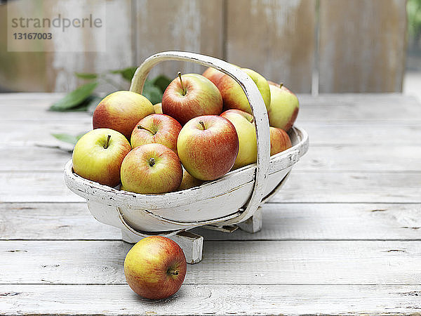 Korb mit Äpfeln auf gekalktem Holztisch