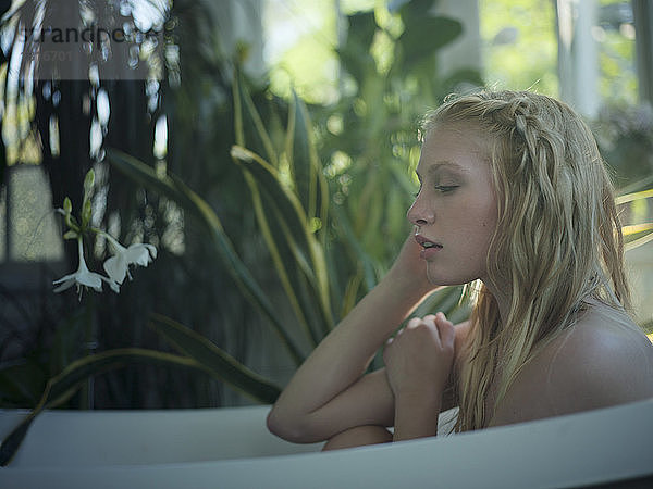 Nackte junge Frau entspannt sich in der Badewanne  im Badezimmer voller Pflanzen