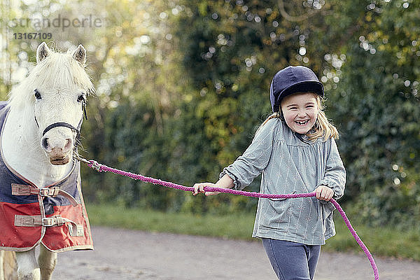 Glückliches Mädchen führt Pony entlang des Feldweges
