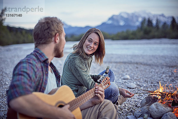 Junges Paar sitzt am Lagerfeuer und spielt Gitarre  Wallgau  Bayern  Deutschland