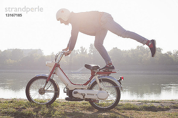 Mittlerer Erwachsener fährt Moped  macht Stunt  am See