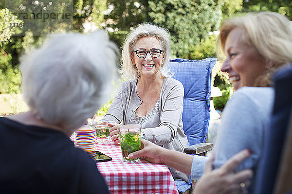 Drei Frauen sitzen im Garten und genießen ein Getränk