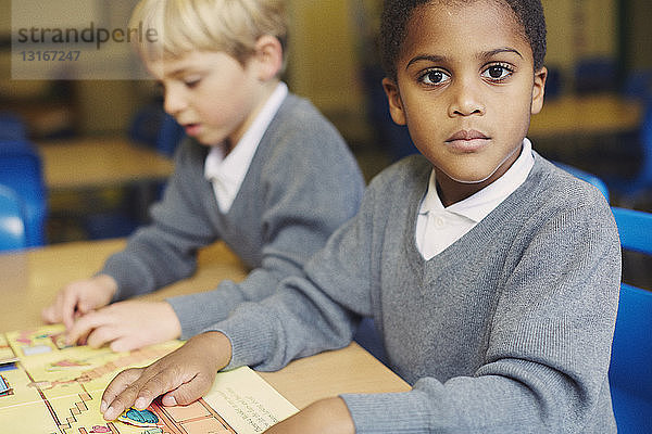 Porträt eines Jungen beim Puzzeln am Schreibtisch im Klassenzimmer der Grundschule