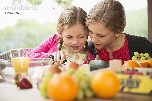 Zwei Schwestern am Terrassentisch lernen  frisches Obst zu schneiden