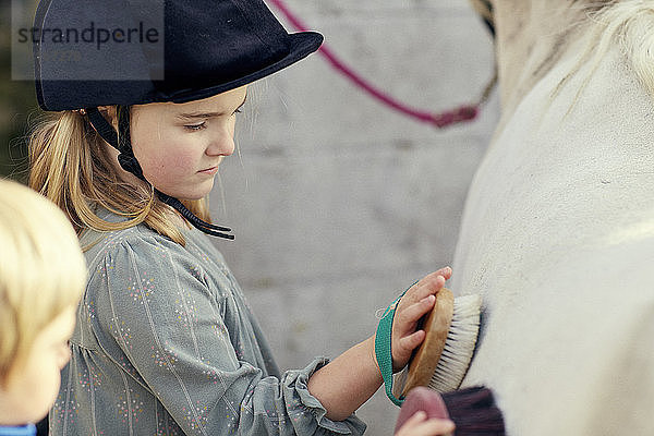 Mädchen und Bruder pflegen Pony im Stall