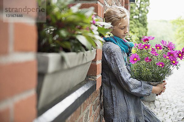 Porträt eines an der Wand lehnenden Mädchens mit Blumentopfpflanze im Garten