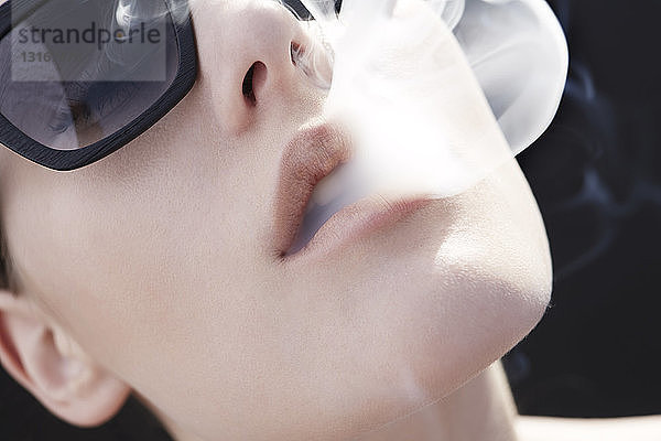 Studiokopfaufnahme einer jungen Frau  die Zigarettenrauch ausatmet