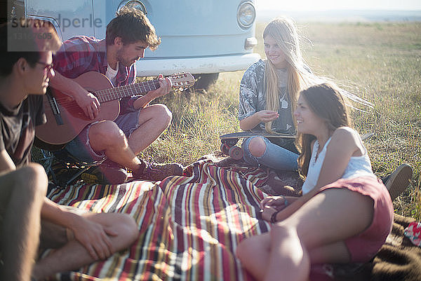Freunde auf Picknickdecke mit Gitarre spielendem Mann