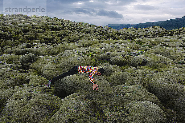 Seitenansicht eines mittleren erwachsenen Mannes  der auf einer hügeligen Vulkanlandschaft liegt  Island