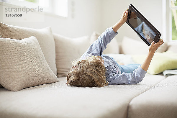 Junge auf dem Rücken liegend auf Sofa mit digitalem Tablett  Arme hochgehoben