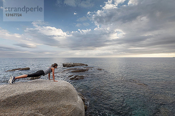Frau auf Felsbrocken mit Blick auf den Ozean