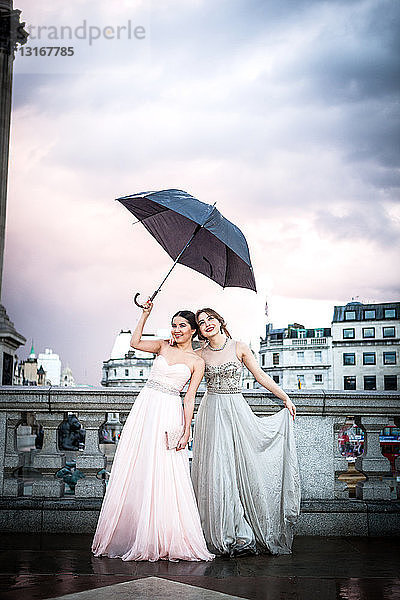 Porträt von zwei weiblichen Models  die einen Regenschirm hochhalten  Trafalgar Square  London  UK