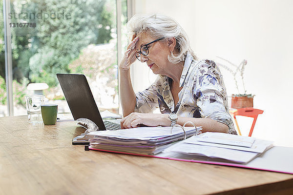 Ältere Frau sitzt am Tisch  benutzt Laptop  besorgter Ausdruck