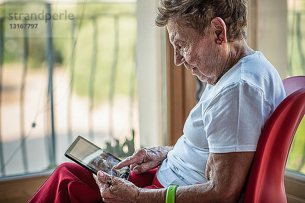 Eine hochbetagte Frau benutzt einen Touchscreen auf einem digitalen Tablett auf dem Balkon ihrer Wohnung