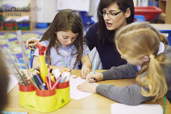 Mädchen und Lehrer zeichnen am Schreibtisch im Klassenzimmer der Grundschule