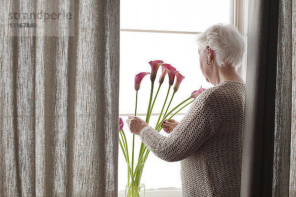 Ältere Frau arrangiert Blumen in Vase  Rückansicht