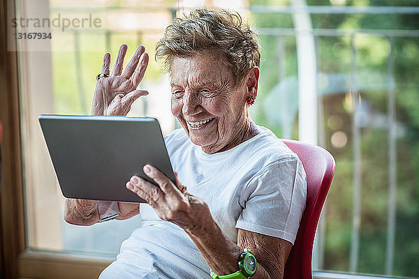 Eine sehr ältere Frau benutzt ein digitales Tablett auf dem Balkon ihrer Wohnung