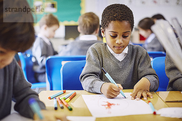 Jungen malen am Schreibtisch im Klassenzimmer der Grundschule