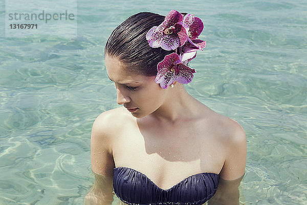 Junge Frau trägt Orchideen im Haar und watet im See