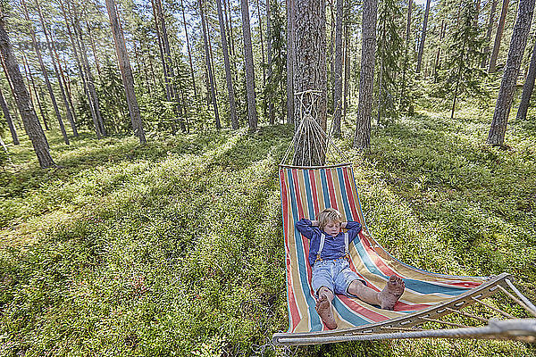 In Retro-Kleidung gekleideter Junge schläft auf Waldhängematte