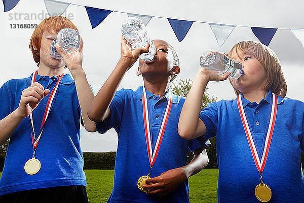 Schuljungen mit Medaillen trinken nach Sportveranstaltung Wasser