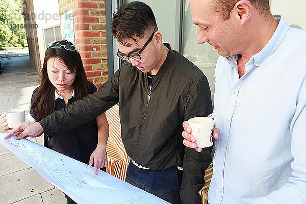 Drei Architektenkollegen inspizieren den Entwurf vor dem Büro