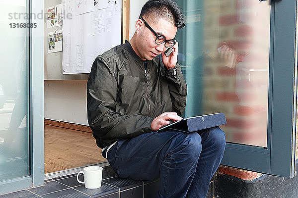 Männlicher Architekt benutzt Smartphone und digitales Tablet auf Bürostufe