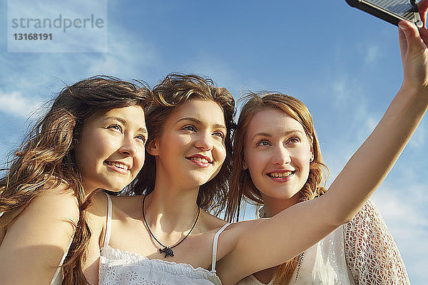 Drei junge Frauen lächeln für Selfie auf Smartphone