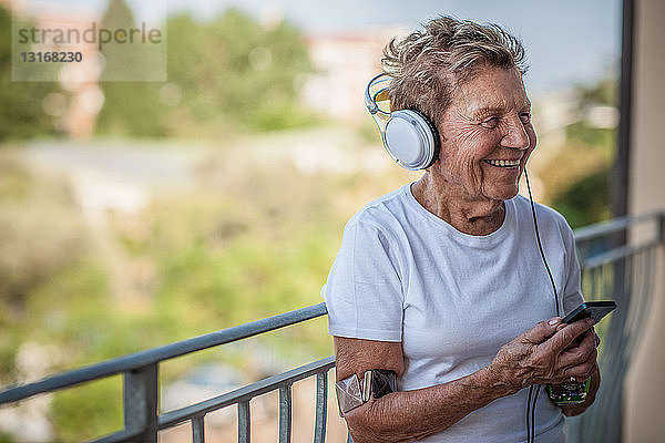 Eine hochbetagte Frau  die auf dem Balkon ihrer Wohnung über Kopfhörer Musik hört