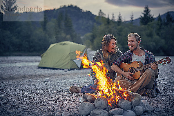 Junges Paar sitzt am Lagerfeuer und spielt Gitarre
