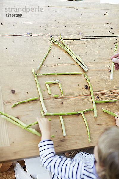 Junge spielt mit Spargel auf dem Esstisch