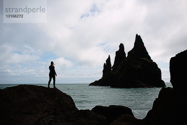 Silhouette einer mittelgroßen erwachsenen Frau  die auf einem Felsen steht und auf den Ozean blickt  Island