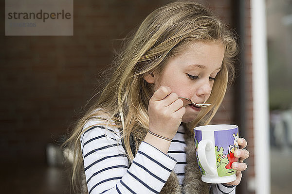 Mädchen löffelt Getränk aus Becher