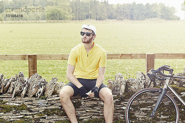 Radfahrer auf Steinmauer sitzend  Cotswolds  UK