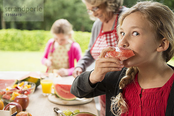 Schelmisches Mädchen am Terrassentisch beim Essen einer Wassermelonenscheibe