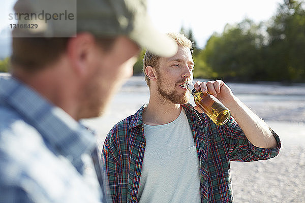 Junger Mann nimmt ein Getränk aus einer Bierflasche  schaut weg