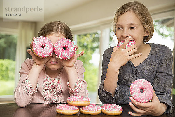 Zwei Schwestern  eine mit Doughnut-Löchern über den Augen  die andere beim Essen