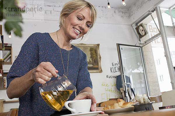 Mittlere erwachsene Frau  die im Café Tee einschenkt