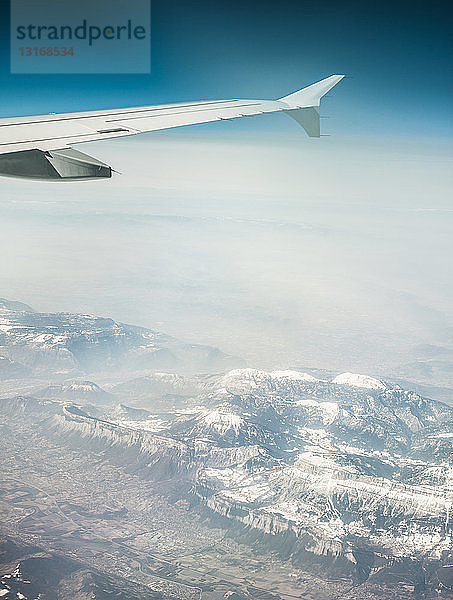 Luftaufnahme eines Flugzeugflügels und nebliger schneebedeckter Berge