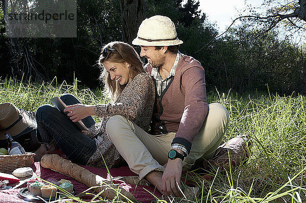 Junges Paar sitzt auf einer Picknickdecke und benutzt ein digitales Tablett