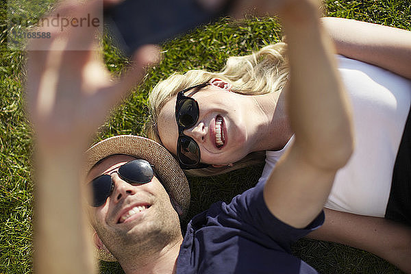 Paar liegt im Park und nimmt sich selbst auf dem Smartphone